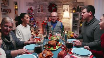 Grandfather sitting at the head of the table for christmas celebration with the family. Traditional festive christmas dinner in multigenerational family. Enjoying xmas meal feast in decorated room. Big family reunion video