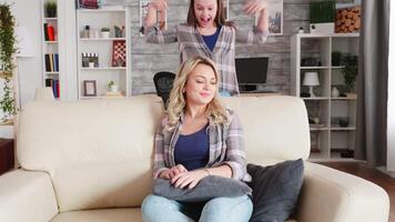 Cute little girl hugging her mother from behind while he's sitting on the couch. video