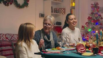 abuela dando su pequeño grandioso hija un regalo a Navidad reunión. tradicional festivo Navidad cena en multigeneracional familia. disfrutando Navidad comida banquete en decorado habitación. grande familia reunión video