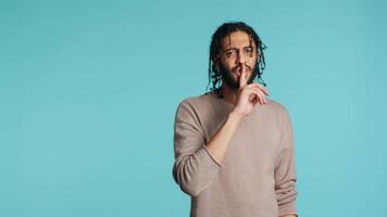 Annoyed middle eastern man doing shushing hand gesturing, irritated by noise, having negative mood. Assertive person placing finger on lips, doing quiet sign gesture, studio background, camera A video