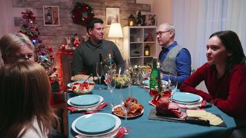 joven madre servicio su familia un sabroso pollo en Navidad reunión. multi Generacion familia. tradicional festivo Navidad cena en multigeneracional familia. disfrutando Navidad comida banquete en decorado habitación. grande familia reunión video