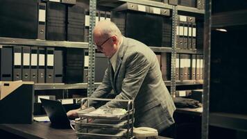 Senior private agent working on criminal report with classified data, searching for old case files to cross check information in archive room. Detective examines legal files and notes. Camera B. video