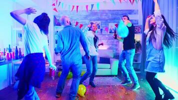 vrolijk en jong groep van mensen dansen in een leven kamer met neon licht. video