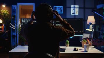 Technician putting headphones on while using coding to fortify firewalls, teleworking for IT company. Computer scientist listening music and upgrading binary code scripts in home office, camera B video