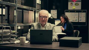 Senior detective asking his partner about legal documents in archive room, looking into crime trends and statistical data to connect different cases. Inspector examines legal statements. Camera B. video