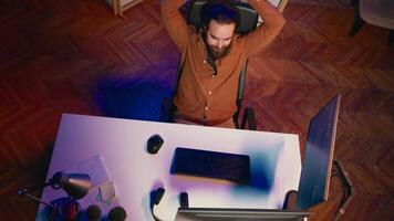 Haut vers le bas vue de il administrateur dans Accueil Bureau élongation après séance sur bureau chaise tout journée. Logiciel ingénieur relâchement en haut, relaxant après dactylographie sur ordinateur pour longue période de temps, aérien coup video