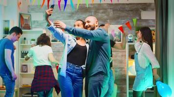 Cheerful bald man taking a selfie with his attractive friend at the party. Using smartphone. video