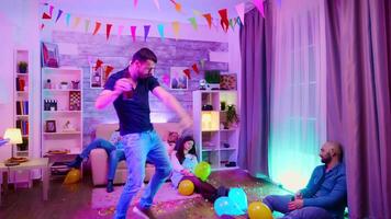 Tired group of people lying on the floor at the party while young man is dancing alone. Neon lights on the wall and disco ball video