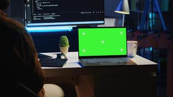 Green screen laptop next to freelancing man doing IT support job from apartment office, coding on PC. Mockup notebook on desk where software engineer writes lines of code on computer at home, camera A video