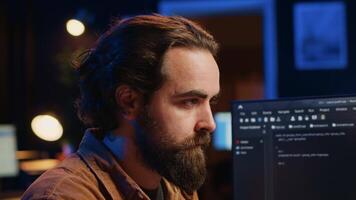 Focused software developer in home office doing coding on computer at desk, close up. IT specialist paying close attention to screen, writing lines of code at workstation, camera A video