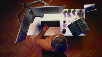 Top down shot of technician focused on typing complex code in home office, developing software application. It specialist removing headphones to better concentrate on difficult task, aerial shot video