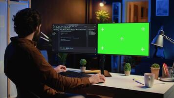 Programmer typing complex code on green screen computer in neon lit home office, developing software application. Teleworking IT specialist doing remote project tasks on mockup PC monitor, camera B video