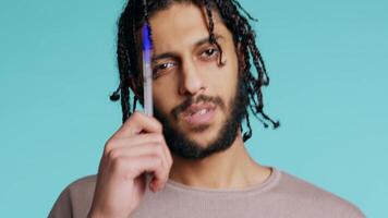 Portrait of man deliberating, putting pen on lips, coming up with idea concept. Thoughtful person reflecting, doing brainstorming, having eureka moment, studio background, camera B close up video