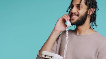 middle eastern man chatting with best friend over telephone call. Upbeat person talking with mate using landline phone, isolated over studio background, camera B close up video