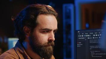 Software technician in apartment office deeply immersed in coding on computer at desk, close up. IT freelancer absorbed by work, focused on screen, writing lines of code at workstation, camera A video