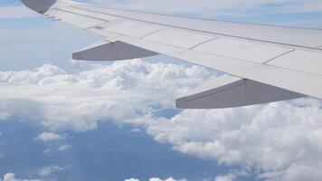 view through aircraft window with plane's wing over blue sky with white fluffy clouds from airplane flight fly over the clouds in a sunny day with cloud moving video