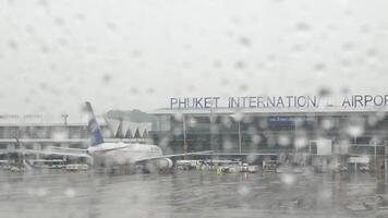 close up selective focus of rain drops on the window surface of the plane in rainy typhoon weather season daytime with Phuket airport terminal video