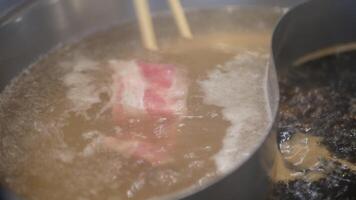 Close up of hotpot shabu with vegetale while using chopsticks putting meat beef sliced to cook in boiling hot pot soup. Japanese asian delicious healthy hotpot shabu food video