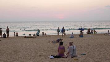 beaucoup gens relaxant sur plage en train de regarder coucher du soleil le coucher du soleil à Karon plage avec magnifique le coucher du soleil d'or vanille ciel, phuket tropical île vacances vacances dans 4k vidéo video