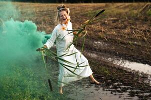 Cheerful young  woman with reeds dances in colored smoke in a field photo