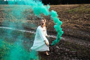 Cheerful young  woman with reeds dances in colored smoke in a field photo