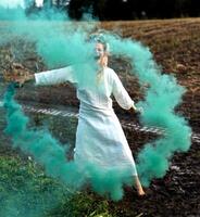 Cheerful young  woman with reeds dances in colored smoke in a field photo