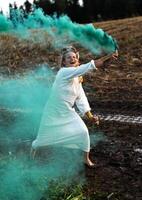 Cheerful young  woman with reeds dances in colored smoke in a field photo