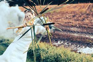 Cheerful young  woman with reeds dances in colored smoke in a field photo