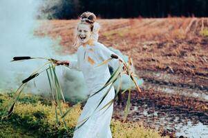 Cheerful young  woman with reeds dances in colored smoke in a field photo