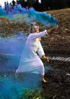 Cheerful young  woman with reeds dances in colored smoke in a field photo