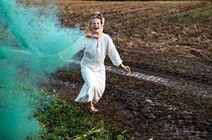 Cheerful young  woman with reeds dances in colored smoke in a field photo