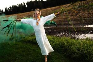 Cheerful young  woman with reeds dances in colored smoke in a field photo