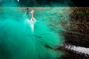 Cheerful young  woman with reeds dances in colored smoke in a field photo