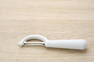 Vegetable Peeler white colored on wooden table, copy space photo