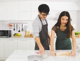 asiático Pareja Cocinando Pizza en moderno cocina, corte un Pizza y sonriente juntos. foto