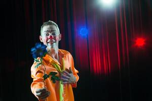 Circus clown performs number. A man in a clown dress with a flower photo