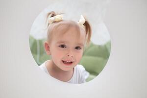 The face of a funny little girl who is looking into a hole made of paper. photo