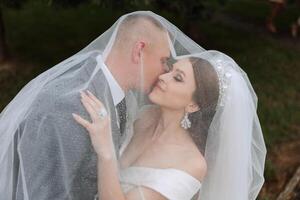 Close-up portrait of two people in love. An affectionate groom embraces the bride, supporting her under the veil. The best moments of the wedding. photo