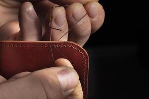 Making leather wallets. The hands of the master sew a leather product. photo