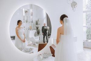 The bride is dressed in an elegant lush white wedding dress with a long veil and is ready for her groom. The first meeting of the bride and groom photo