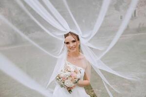 portrait of a beautiful young bride in a white dress with a long veil and a gorgeous hairstyle. Smiling bride. Wedding day. Gorgeous bride. Marriage. photo