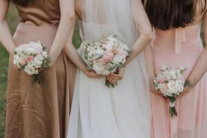 The bride and her two friends turned their backs to the camera, holding wedding bouquets of flowers behind their backs. photo