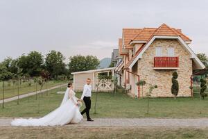 A handsome groom and an elegant bride in a lush white dress are walking in a summer park. Happy bride and groom getting ready for their best day. photo