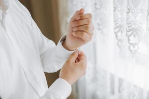 Hands button up the buttons on his shirt. The process of fastening the buttons on his white shirt. Close view. Groom buttons on his shirt cuffs. Morning of the groom photo