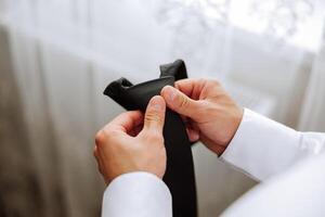 A bearded man in a white shirt adjusts his tie. Groom's morning. Close-up detail, men's tie for a wedding or an important meeting. photo