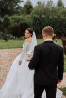 The bride is dressed in an elegant lush white wedding dress with a long veil and is ready for her groom. The first meeting of the bride and groom photo