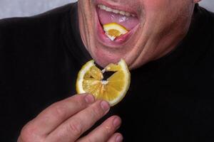 An unrecognizable man eats a sour lemon. photo