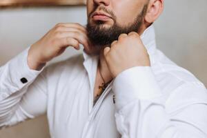 negocio camisa. un hombre en un blanco camisa sujeta el botones. joven político, masculino estilo, empresario abotonarse camisa, masculino manos de cerca, americano, europeo empresario foto