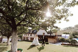 A handsome groom and an elegant bride in a lush white dress are walking in a summer park. Happy bride and groom getting ready for their best day. photo