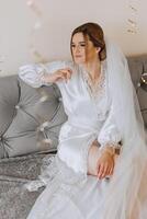 A beautiful bride is sitting in a dressing gown in the morning before the wedding ceremony in a hotel with a modern interior. Incredible hairstyle of the bride. Natural and modern makeup. photo